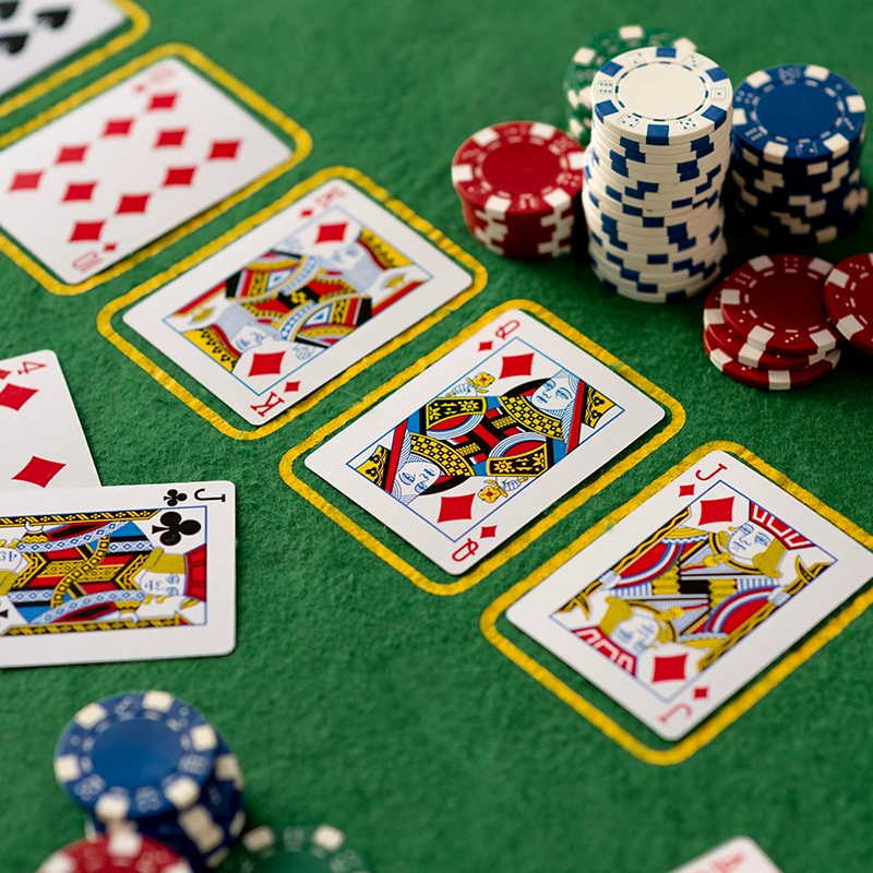 A poker table with face cards and stacks of red, blue, and white poker chips.