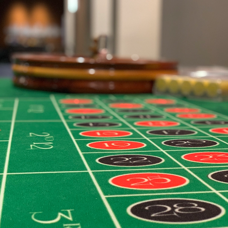 Close-up of a roulette table with numbers in red and black circles, and a roulette wheel in the background.